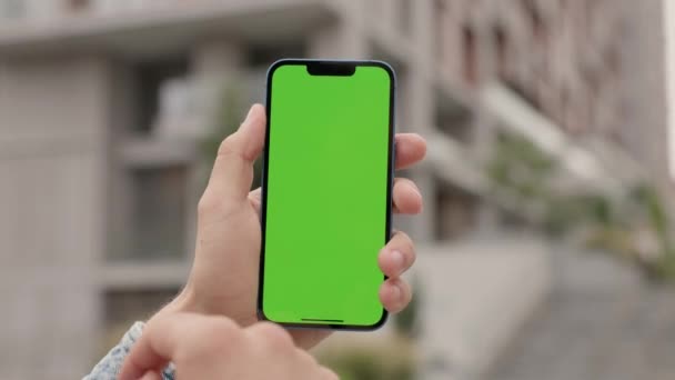 男子手中的垂直绿色屏风在城市建筑背景下的电话近视 盖伊在外面使用智能手机 在Chroma键显示上滚动和触摸 — 图库视频影像