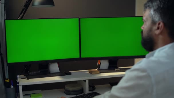 人間のトレーダーかビジネスマンは緑スクリーンのモックアップが付いている2つのモニターが付いている卓上コンピュータで働きます — ストック動画