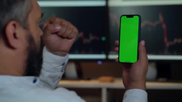 Man Trader Using Phone Green Mock Screen Background Computer Monitors — Stock Video