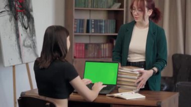 Laptop Green Mock-up ekranlı iki genç kız masanın yanında konuşuyor. Klavye Laptop 'ta Krom Anahtarlı Bilgisayar Ekranı ile Yazan Kız