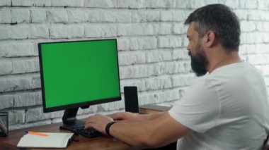 Yeşil Mock Up ekranlı, Masaüstü Bilgisayarı 'nda çalışan sakallı orta yaşlı adam. Beyaz Tuğla Duvarlı Modern Ofis