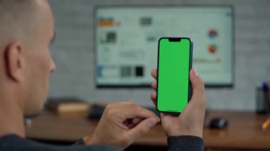 Telefonun Erkek Ellerinde Yeşil Ekran Modeli ile Kapanışı. Adam İş Yeri 'nde Bilgisayarın Yakınındaki Telefonu Kullanıyor