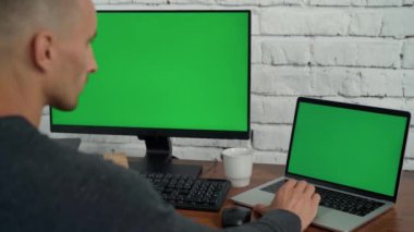 Adam masaüstü bilgisayarında ve ofiste yeşil ekranlı dizüstü bilgisayarda çalışıyor. Bilgisayarda Krom Anahtar ve Dizüstü Bilgisayar Görüntüsü