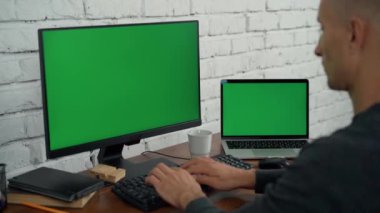 Adam masaüstü bilgisayarında ve ofiste yeşil ekranlı dizüstü bilgisayarda çalışıyor. Bilgisayarda Krom Anahtar ve Dizüstü Bilgisayar Görüntüsü