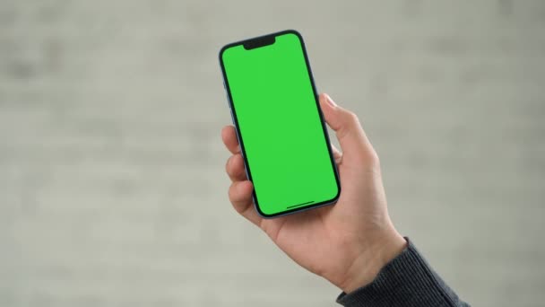 ホワイトウォールの背景に対する男性の手の緑色のスクリーンモックアップとの電話のクローズアップ — ストック動画