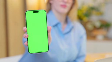 Gülümseyen Genç Kadın Yeşil Ekran Mock Up Ekranı ile Akıllı Telefon Gösteriyor. Arka plan, rahat ev mutfağı.