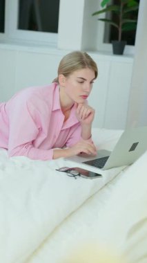 Dikey ekran: dizüstü bilgisayar kullanan genç bir kadın evde yatağında yatıyor. Evde Dinlenen ve Not Defterinde Sosyal Medyayı Denetleyen Kadın