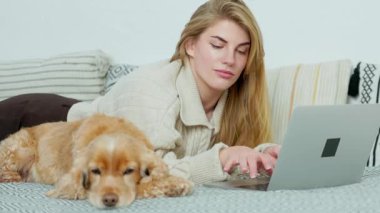 Genç Kadın Evcil Köpeğiyle Kanepede Uzanıyor ve Laptop Kullanıyor. Ev Bilgisayarından Serbest Çalışan ya da Öğrenci Kız Çalışmaları ve Çalışmaları