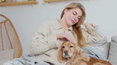 Genç bir kadın evcil köpeğini koltukta rahat bir odada okşuyor. Evcil Hayvan ve Kadın Oturma Odasında Rahatlayın ve Dinlenin