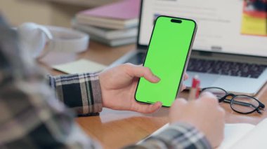 Dikey Yeşil Ekran ile Cep Telefonu Kullanan Genç Adam Not Defterine Bir Şey Yazıyor