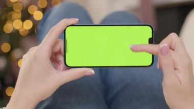 Yeşil Ekranlı Telefonun Yakın plan Çekimi Kadın Elleri Noel ağacının Arkasında ve Bulanık Işıklar. Kadın Kaydırma ve Dokunma Anahtarı Gösterimi Hareketleri Yapıyor