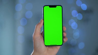 Bulanık ışıklara karşı Erkek Ellerinde Yeşil Model Ekranlı Akıllı Telefonun Yakın Çekimi. Telefon Ekranına Geçiş, Kaydırma ve Tıklama Hareketleri Yapan Kişi