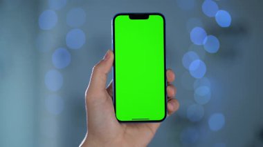 Bulanık ışıklara karşı Erkek Ellerinde Yeşil Model Ekranlı Akıllı Telefonun Yakın Çekimi. Telefon Ekranına Geçiş, Kaydırma ve Tıklama Hareketleri Yapan Kişi