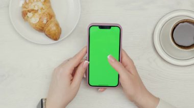 Kadın Ellerinde Yeşil Model Ekranlı Cep Telefonu 'nun Yakın Çekimi. Kafede dinlenirken akıllı telefon kullanan, kahve içen ve kruvasan yiyen bir kadın.