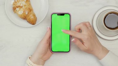 Kadın Ellerinde Yeşil Model Ekranlı Cep Telefonu 'nun Yakın Çekimi. Kafede dinlenirken akıllı telefon kullanan, kahve içen ve kruvasan yiyen bir kadın.