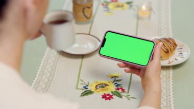 Kadın Ellerinde Yeşil Model Ekranlı Cep Telefonu 'nun Yakın Çekimi. Kafede dinlenirken akıllı telefon kullanan, kahve içen ve kruvasan yiyen bir kadın.