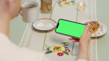 Kadın Ellerinde Yeşil Model Ekranlı Cep Telefonu 'nun Yakın Çekimi. Kafede dinlenirken akıllı telefon kullanan, çay içen ve kruvasan yiyen bir kadın.