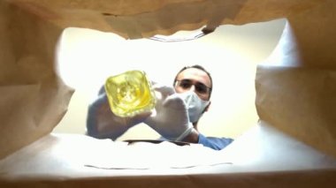 Maskeli ve eldivenli bir adamın kağıt torbasının içinden eve yemek tıkıştırdığı görüntüler.