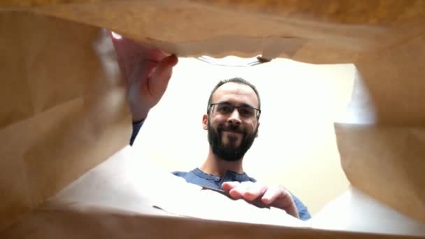 家で食べ物を取る髭の男と眼鏡の紙袋の中からの眺め — ストック動画