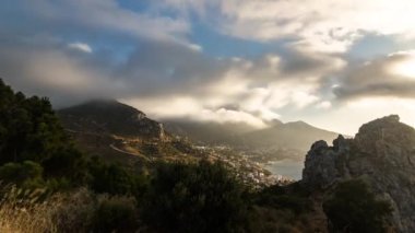 Dağlardan geçen bulutlar ve gün batımında bir kasaba