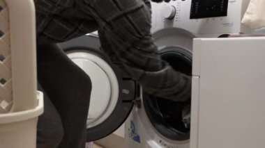 Man in pajamas putting dirty clothes in the washing machine at home