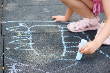 Renkli tebeşirle oyun parkının zeminine resim çizen tanınmamış küçük kız..