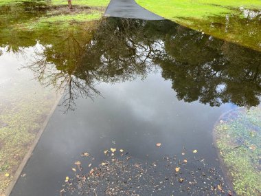 Flooded pedestrian walkway after heavy rain. Trees reflect on water.