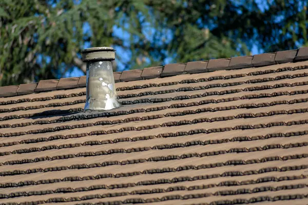 stock image A weathered metal roof vent with peeling paint is set on top of a brown, textured shingle rooftop.