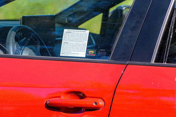 Proposition 65 warning label is attached to the driver side window of a red car - California, USA - September 30, 2024