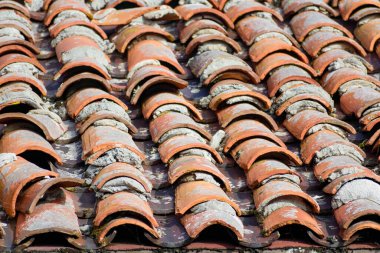 Düz olmayan ve çatlamış kiremitleri olan yaşlanmış terracotta kiremit çatısı, fayansların arasında aşınma izleri ve havan topları gösteriyor..