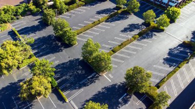 Yeşil ağaçlar ve çalılarla çevrili boş bir otoparkın havadan görünüşü, işaretli park yerleri ve sürüş şeritleri..