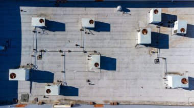 Endüstriyel HVAC üniteleri olan bir binanın düz çatısının havadan aşağı görüntüsü.
