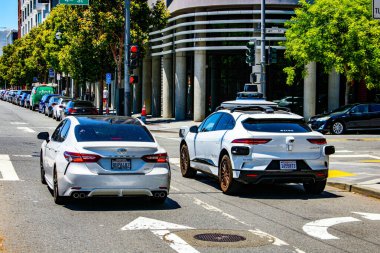 Trafik ışıklarında iki araç: beyaz bir sedan ve kendi kendine giden çatı sensörlü Waymo Jaguar - San Francisco, California, ABD - 22 Haziran 2024