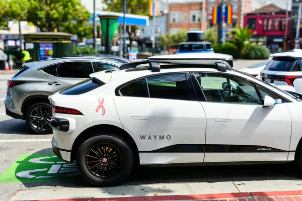 Beyaz bir Waymo kendi kendini süren Jaguar I-PACE, pembe göğüs kanseri farkındalığı kurdelesiyle süslenmiş, arka planda diğer araçlar - San Francisco, California, ABD - 13 Temmuz 2024
