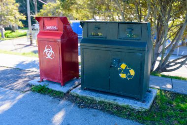 Kırmızı bir biyolojik tehlike kutusu, yeşil bir çöp kutusu ve beton bir platformda geri dönüşüm kutusu. Kapat..