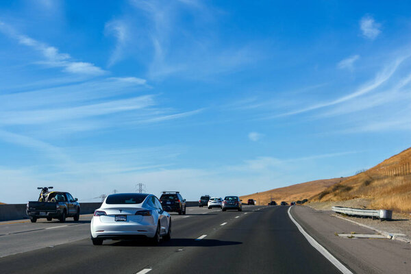 Vehicles on Highway 101 northbound move along a sunny stretch of road surrounded by golden hills and open skies - San Jose, California, USA - October 20, 2024
