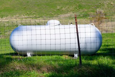 Endüstriyel propan depolama tankı kırsal alanda metal bir çitle korunuyor..