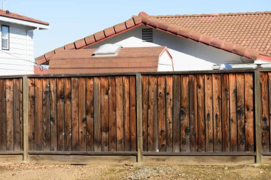 A weathered wooden fence stands in the foreground, with residential rooftops featuring red tiles and white siding visible under a clear blue sky clipart