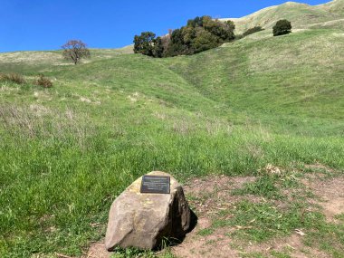 Boccardo Patikası adlı bronz bir plaket ön planda duruyor. Yuvarlanan tepeler ve dağınık ağaçlar San Jose, California, ABD - 1 Mart 2025