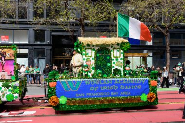 İrlanda temalı tören şamandırası üzerinde Whelan İrlanda Dansı Akademisi afişi bulunan yonca ve leprikon figürleriyle süslenmiş San Francisco, California, ABD - 15 Mart 2025