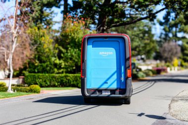 Amazon elektrik dağıtım minibüsü bir banliyö caddesi boyunca sürüyor. Arkadan bak. Seçici odak - Kaliforniya, ABD - 2 Mart 2025