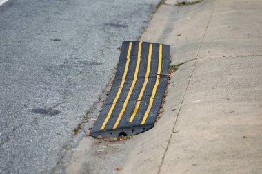 Lastik kaldırım köprüsü, sarı çizgili rampa beton bir garaj yolu ile asfalt yol arasındaki oluklar üzerine kurulmuş. Kapat..