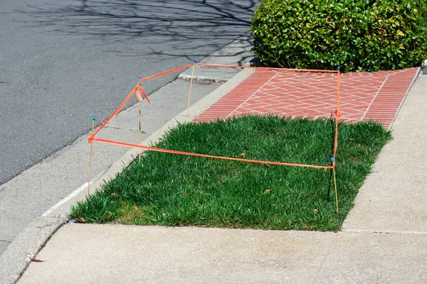 Güneşli bir günde etrafı beton ve budanmış çitlerle çevrili, turuncu bantlarla korunan kare çimenli bir bölümü olan yerleşim yeri..