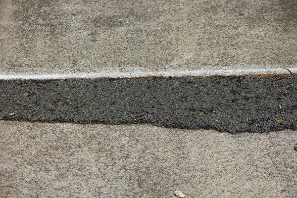 Düz olmayan asfalt yamasıyla beton kaldırıma yakın çekim.