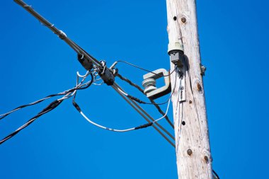 Çoklu siyah beyaz yalıtımlı kabloları destekleyen yıpranmış elektrik direği. Kapat.