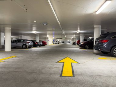 Yeraltı otoparkı, beton sütunlar, parlak tepelik aydınlatma ve birkaç park etmiş araba. Sarı yönlü ok rehberli araçlar - Kaliforniya, ABD - 3 Haziran 2025