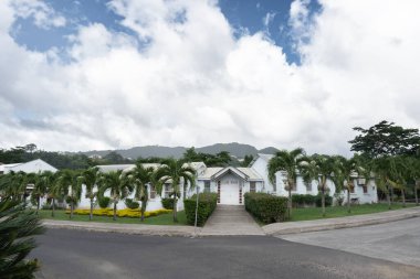 Beyaz, bir kat beyaz bina. Önünde palmiye ağaçları, arkasında dağlar.