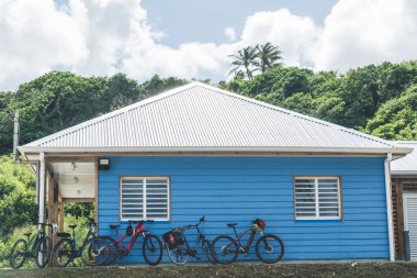 Duvara dayanmış 5 bisikletli tropikal bir köyde mavi bir bina.