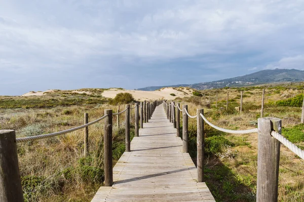 Sintra 'da Praia do Guincho plajındaki boş tahta kaldırım. Arkasında tepeler ve Atlantik Okyanusu olan çimen ve kum manzarası