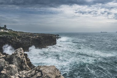 Cascais, Portekiz 'deki Atlantik Okyanusu kıyısında. Dalgalar kıyıda ve kayalık tepelerde